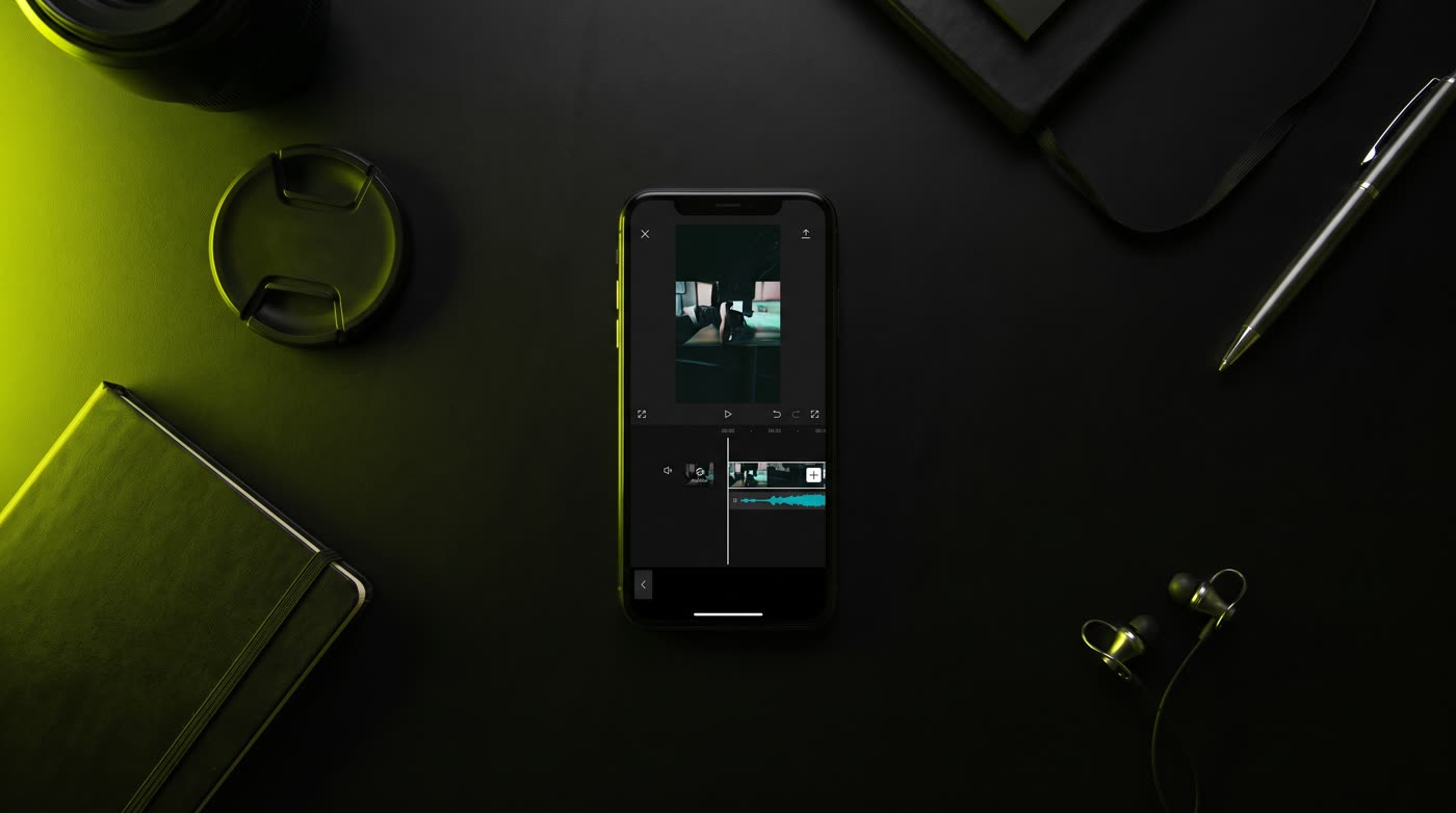Overhead flat lay of a phone showing a vertical video timeline on a matte black desk
